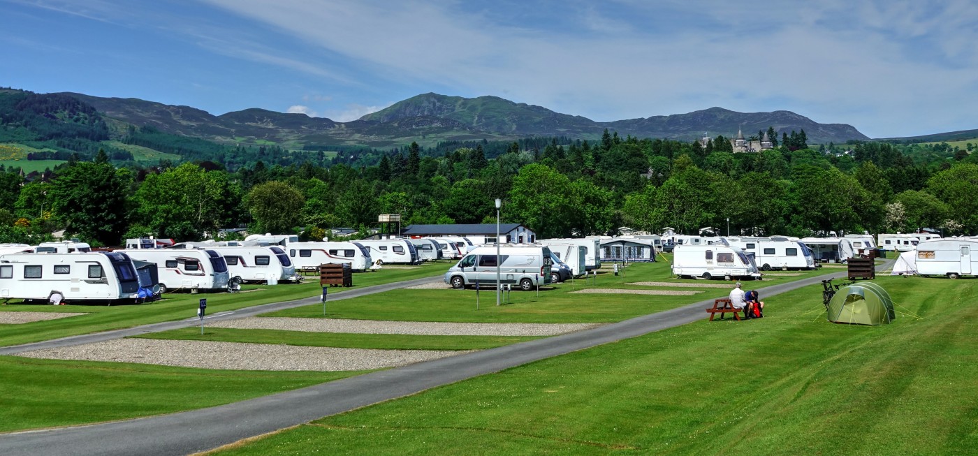 overview of Fonab caravan park with touring caravans and motorhomes. Deep green bushes and rolling hills in the background with the peaks of Atholl Palace in amongst the foliage
