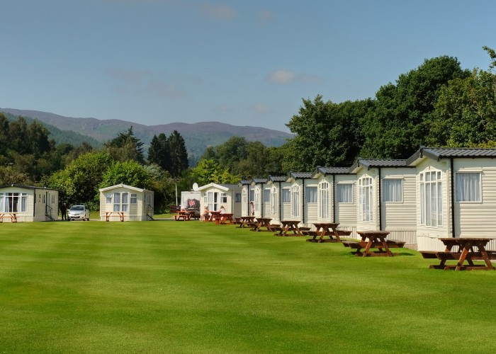 Large open grassy area in the middle of static caravans with individual picnic benches for each static holiday home.