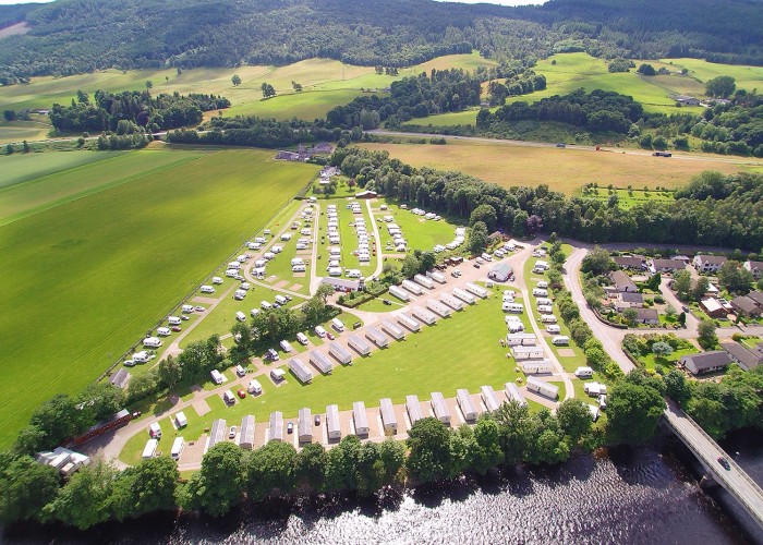 Ariel view of Fonab Caravan Park from the River Tummel. Bright green grass takes centre amongst the static homes and tourer campers are parked on site in the second field. Surrounded by deep green trees and farmlands.